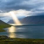 sun reflection on calm water near green mountains